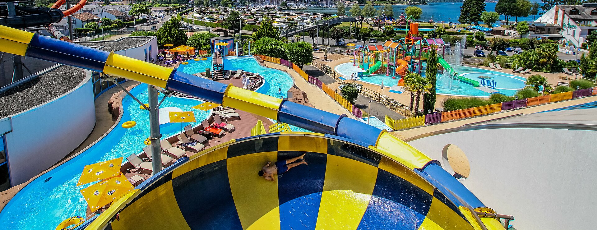 Au premier plan un homme dans le toboggan la Tornade d'Aquaparc. Au second plan une vue sur la lazy river d'Aquaparc et sur le lac léman