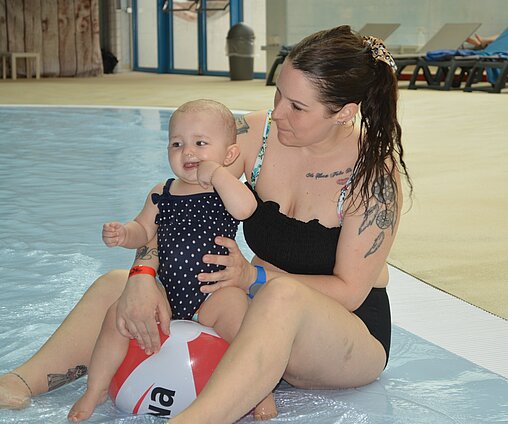 Une maman avec un bébé dans les bras au bord de la piscine à vagues d'Aquaparc